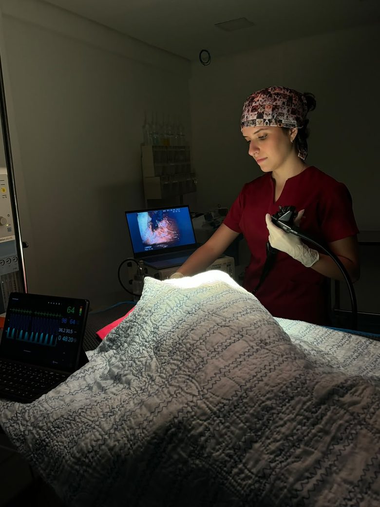 Raphaella Martins conduzindo uma endoscopia, com o monitor do exame e a monitoração do paciente ao lado