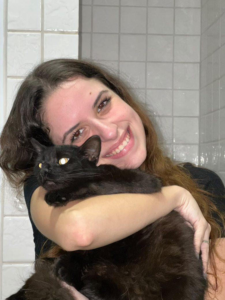 Raphaella Martins sorrindo e abraçando um gato preto